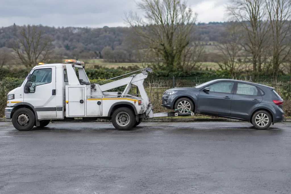 A wheel-lift recovery truck carrying the front wheels of a small car